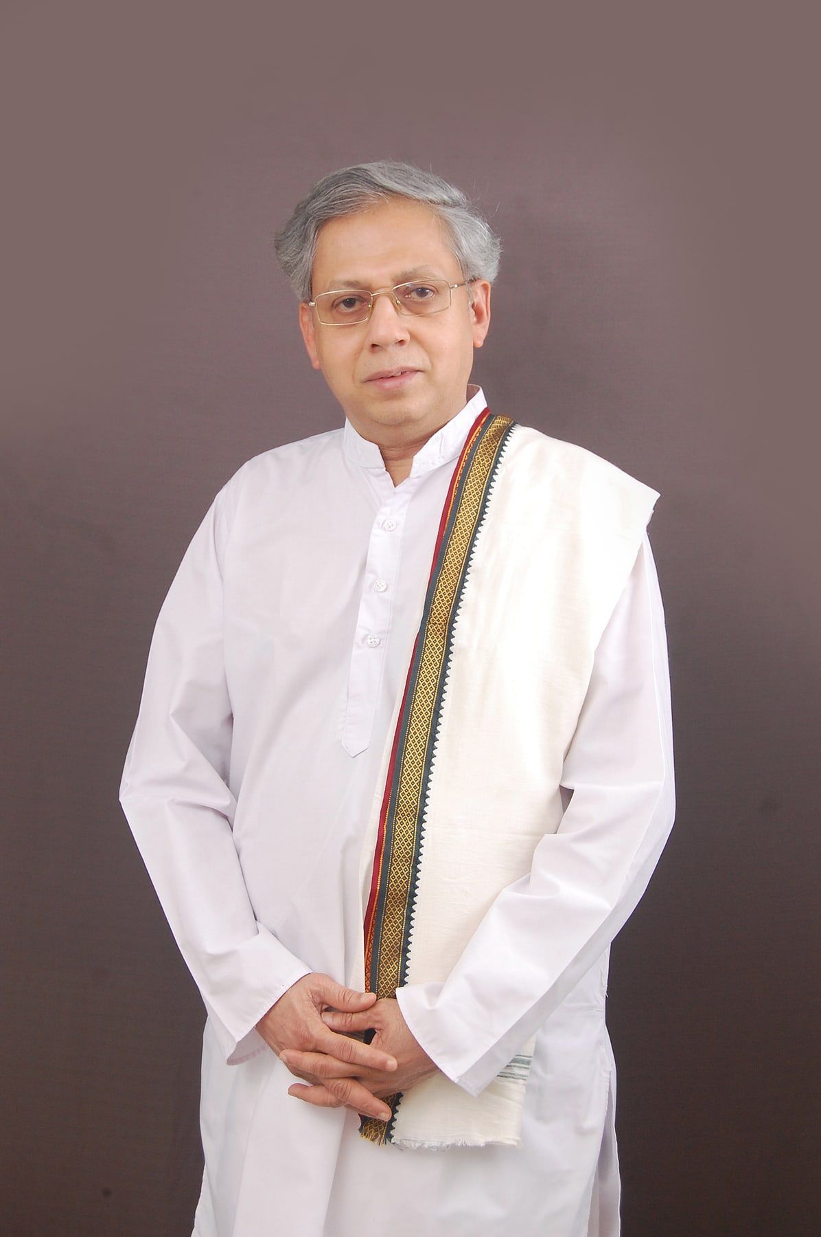 Neelakanth Phadke standing in a white kurta and an uparne with a woven border, against a plain dark ground.
