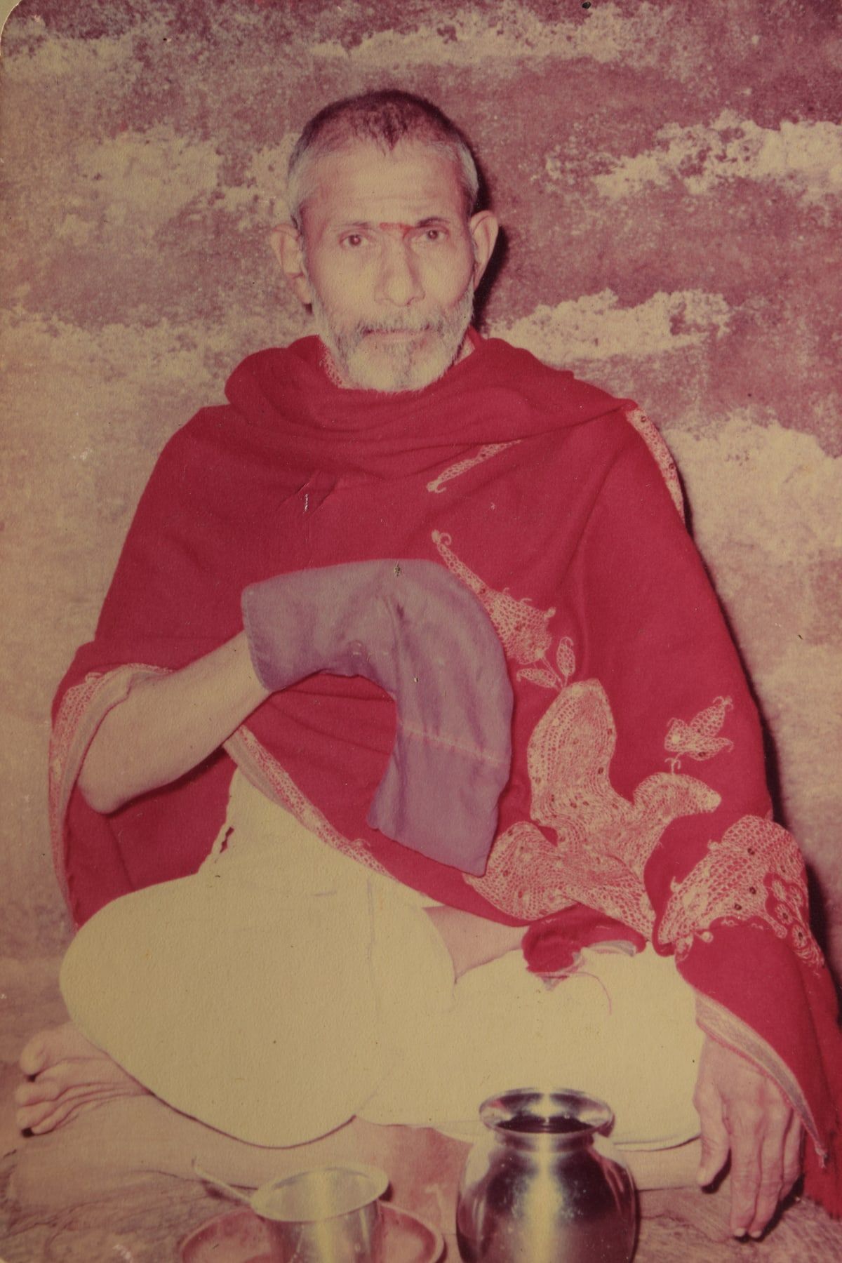 Pundit Purushottamshastri Phadke in 1973, seated cross-legged in a red shawl against a weathered wall.